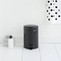 Schwarzer Tretmülleimer in einem weißen Badezimmer neben einem Seifenspender und einem gemusterten Behälter, mit einem Handtuch mit Polka-Dot-Muster in der Nähe.