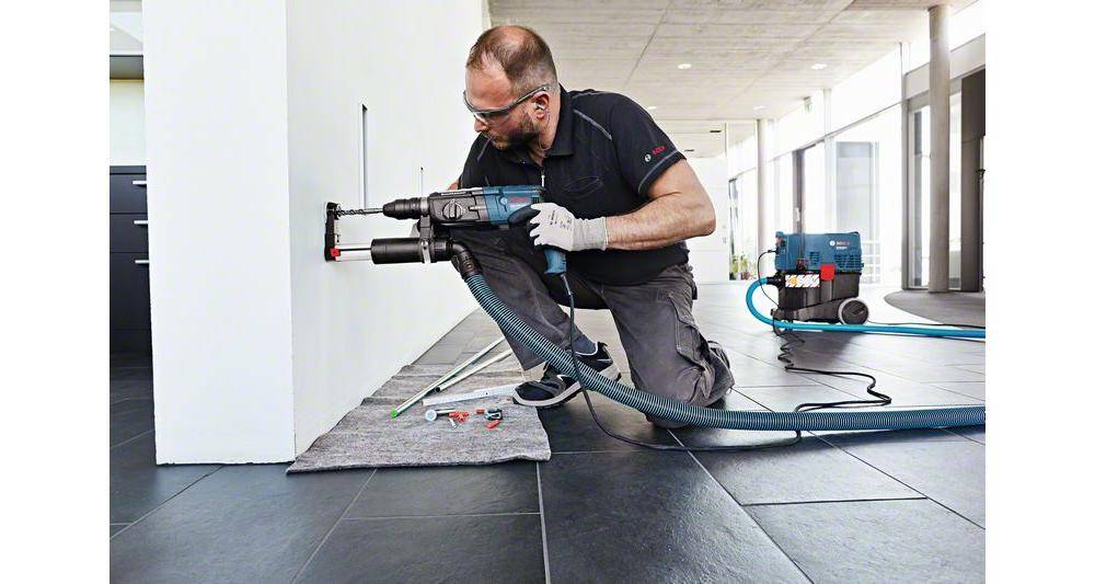 Eine Person mit Sicherheitsausrüstung bohrt mit einem Akkuschrauber ein Loch in eine Wand in einem modernen Raum.