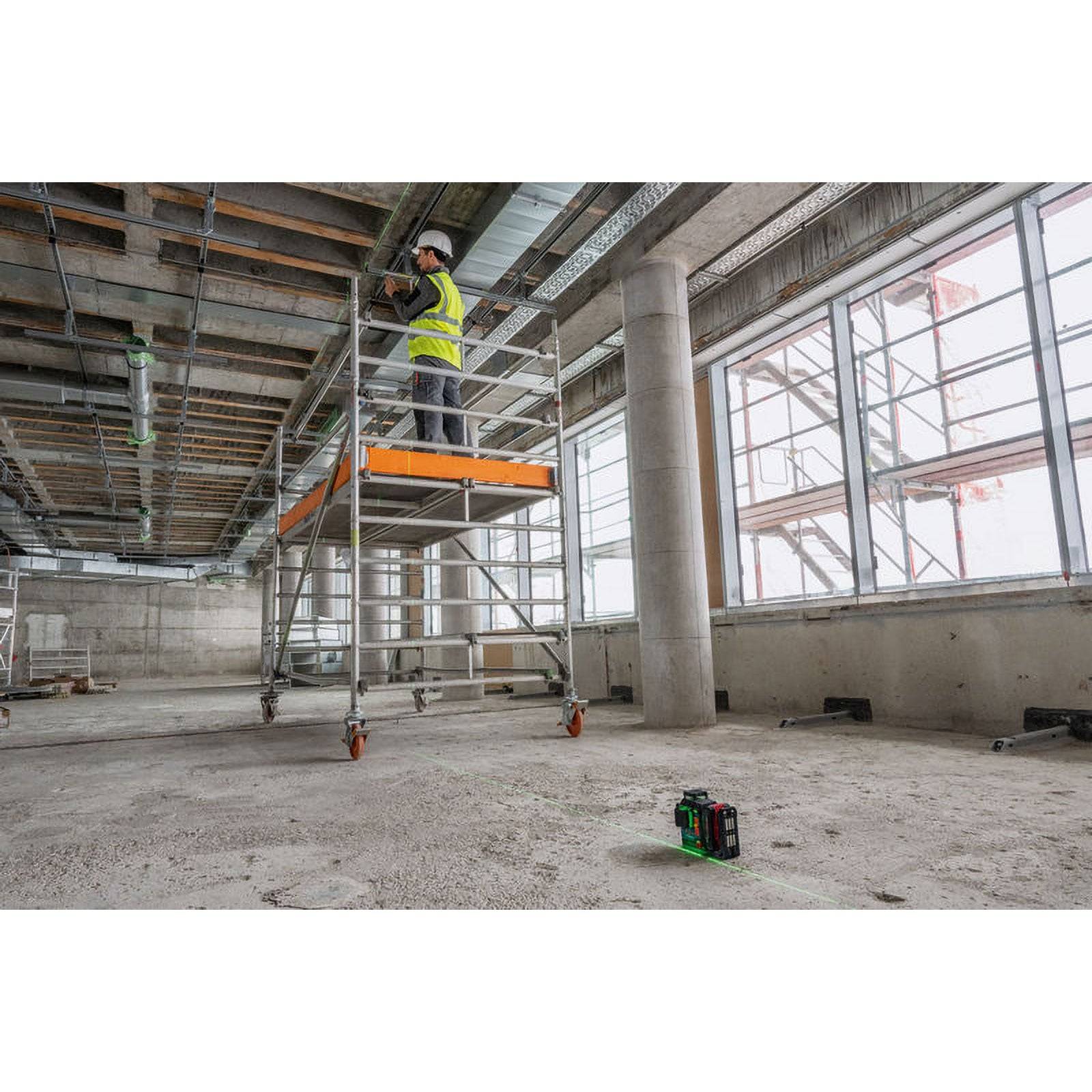 Ein Arbeiter mit Warnweste und Helm steht auf Gerüsten in einem großen, unfertigten Gebäude und arbeitet mit Werkzeugen an der Decke.