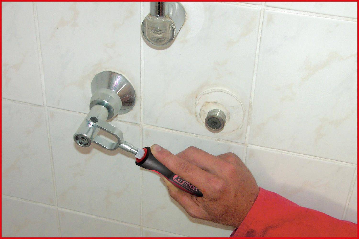 Eine Hand benutzt einen Innensechskantschlüssel, um einen Duscharmatur einzustellen. Die Fliesen und die Beschläge deuten auf eine Badezimmerumgebung hin und unterstreichen eine Reparaturaufgabe.