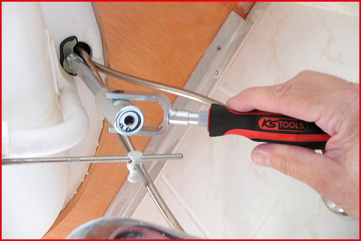 Eine Hand hält einen KS Tools Ratschenschlüssel, der eine Rohrverbindung unter einem Waschbecken anzieht, und zeigt Sanitär-Reparatur- oder Wartungsarbeiten.