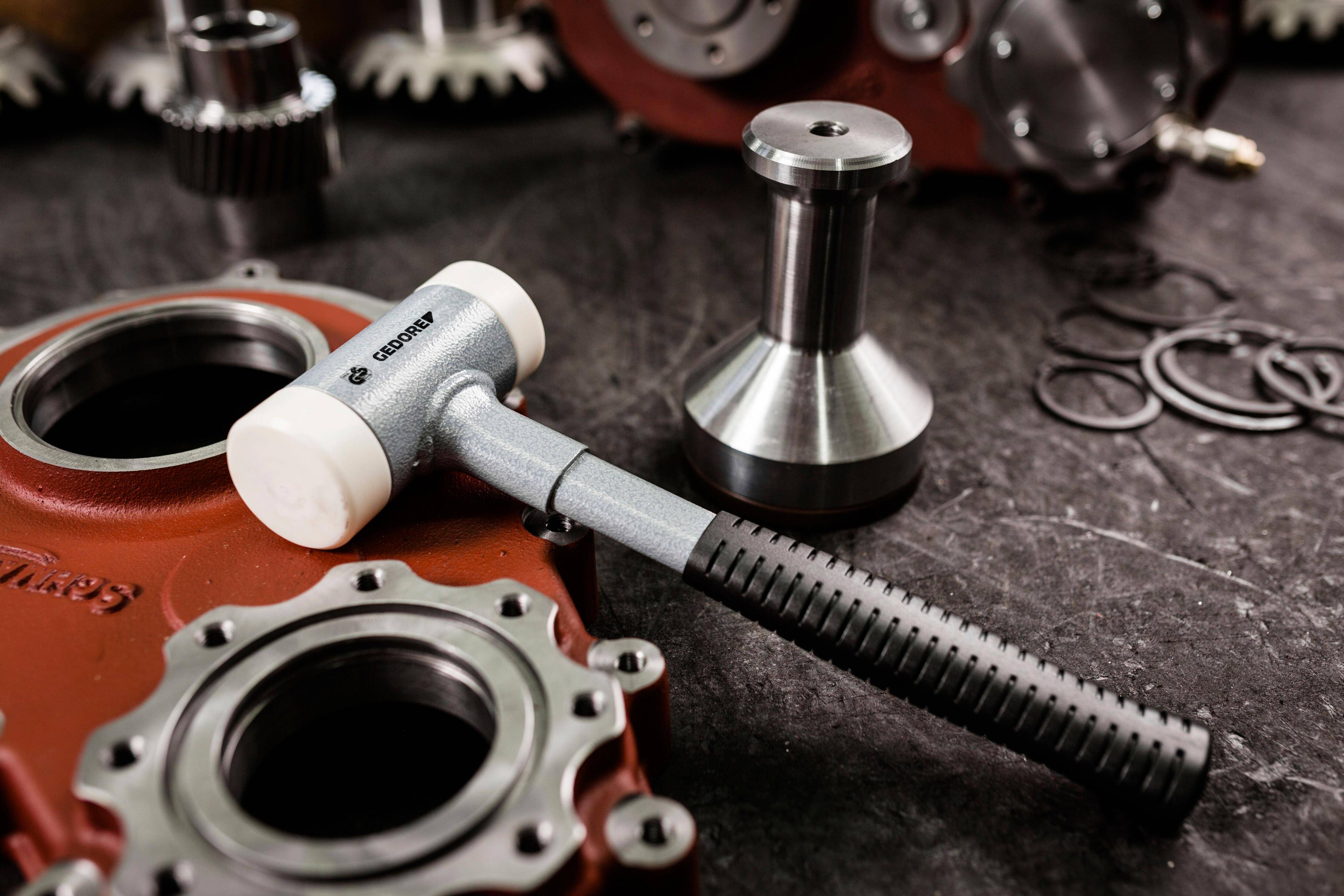 Eine Metallwerkbank, auf der ein Gummihammer neben verschiedenen Maschinenteilen angebracht ist, was auf eine Werkstatt oder eine Metallearbeitungsumgebung hindeutet.