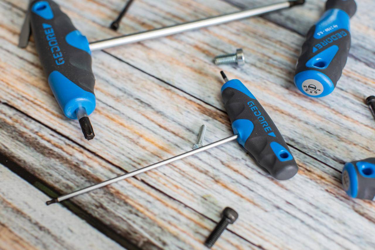 Ein Set aus blauen und schwarzen Schraubendrehern auf einer Holzoberfläche, mit verschiedenen verstreuten Schrauben, was auf eine Montage- oder Reparaturaufgabe hindeutet.