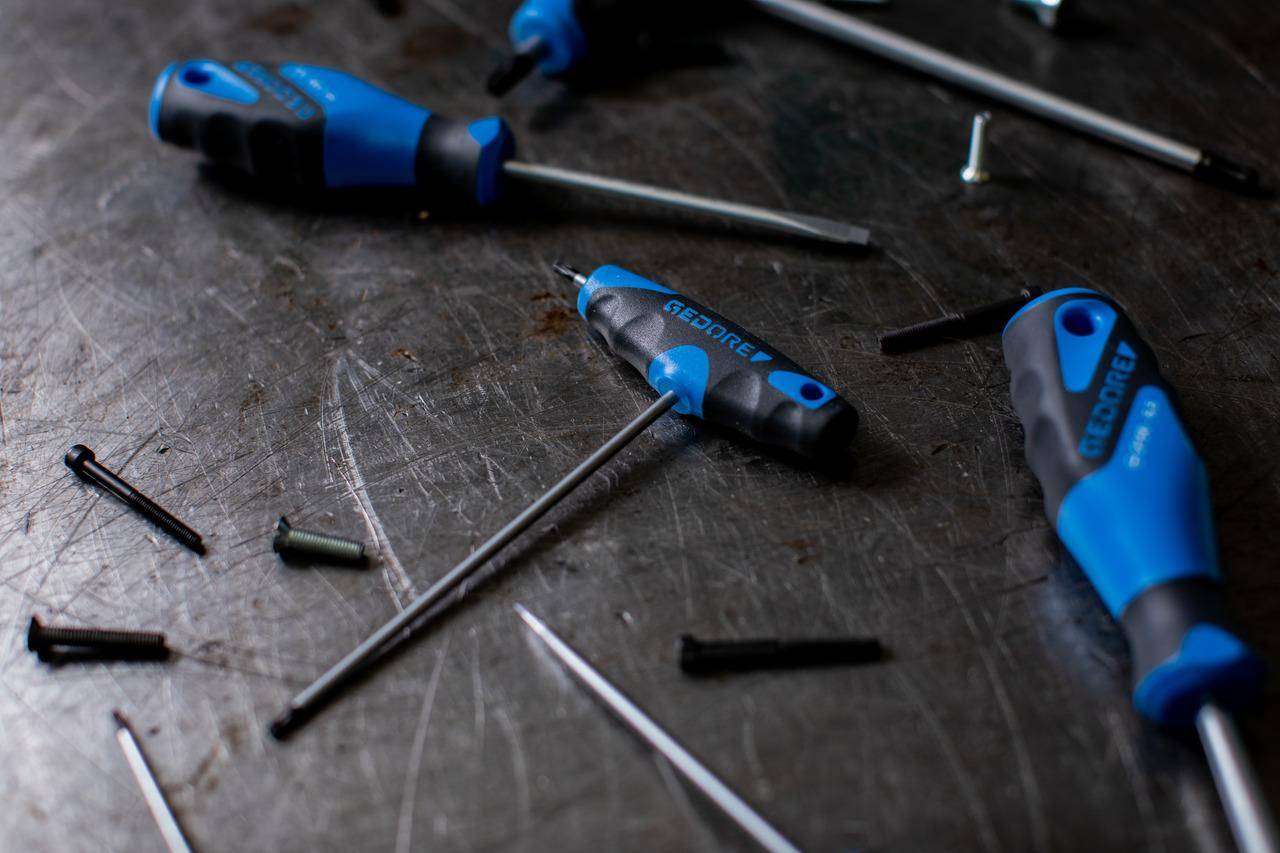 Blau und schwarz gestielt Schraubendreher verstreut auf einer Metallfläche mit Schrauben in der Nähe.