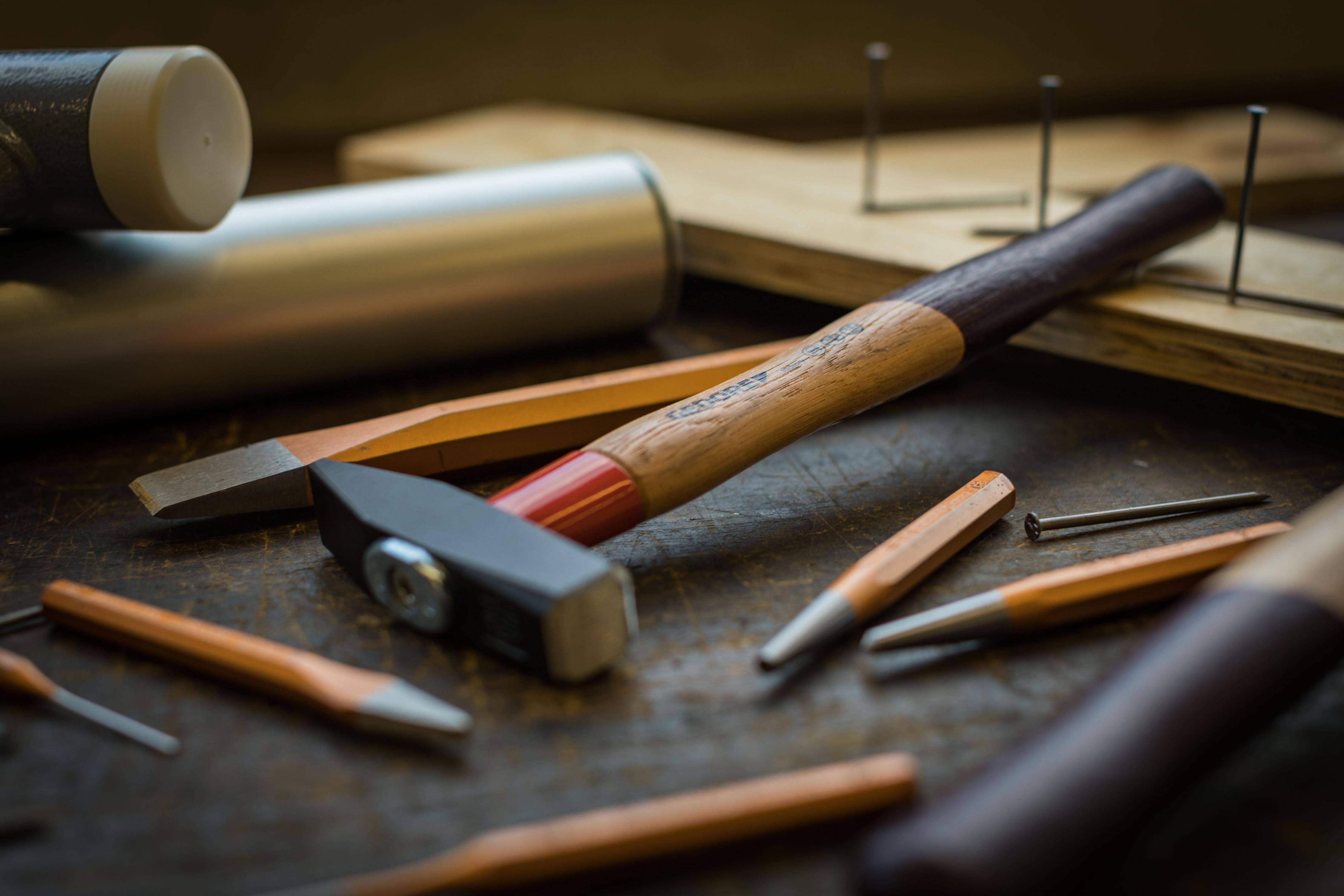 Holzbearbeitungswerkzeuge, einschließlich eines Hammers, eines Meißels und eines Holzblocks, sind auf einer Werkbank angeordnet und deuten auf handwerkliche Aktivität hin.