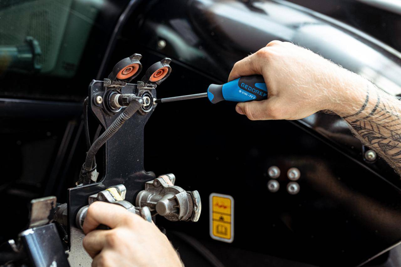 Eine Person verwendet einen Schraubendreher, um ein Teil an einer Maschine einzustellen, wobei sie sich auf mechanische Komponenten und elektrische Verbindungen konzentriert.