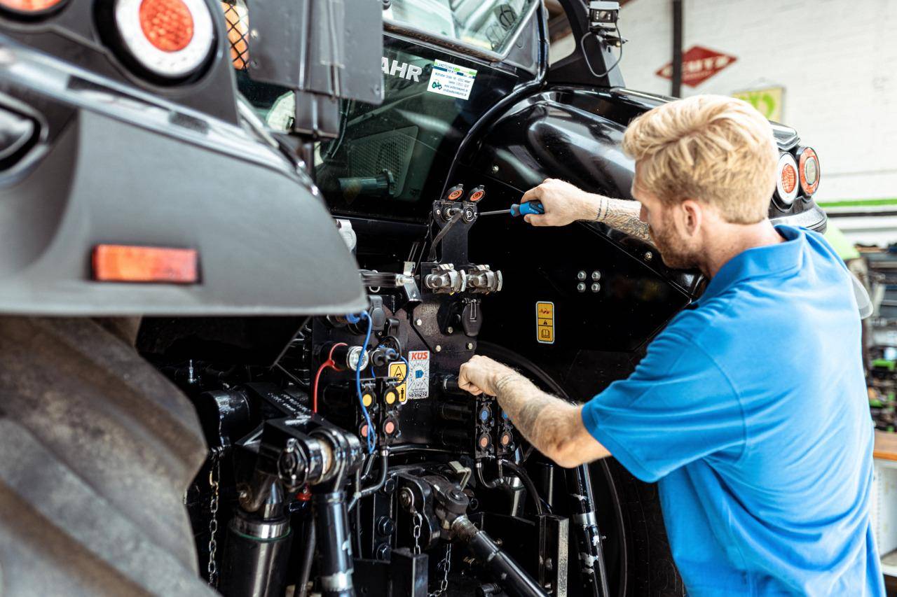 Eine Person in einem blauen Hemd benutzt Werkzeuge, um Komponenten an schweren Maschinen in einer Werkstattumgebung einzustellen.