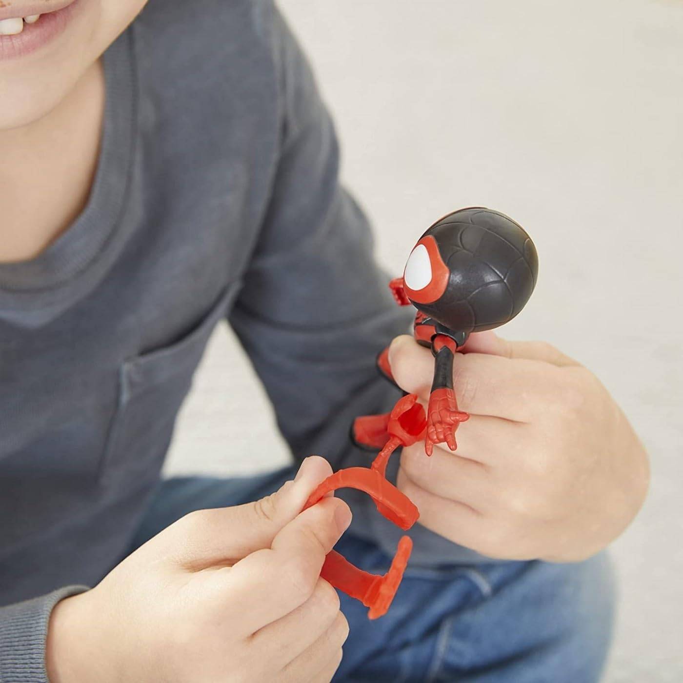 Kind hält eine kleine rot-schwarze Spider-Man-Figur und stellt deren Teile ein, während es drinnen sitzt.