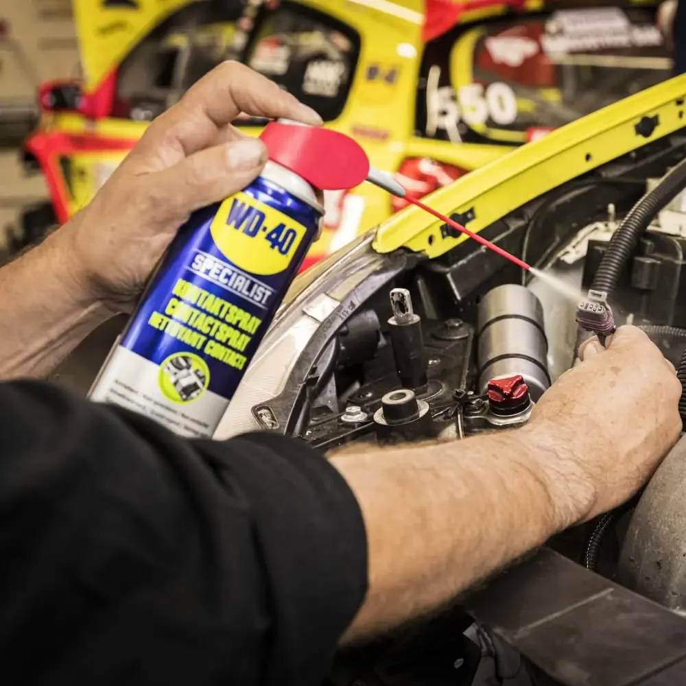 Mechaniker sprüht WD-40 Specialist Elektrokontakt-Reiniger auf einen Automotor-Stecker in einer Werkstatt.