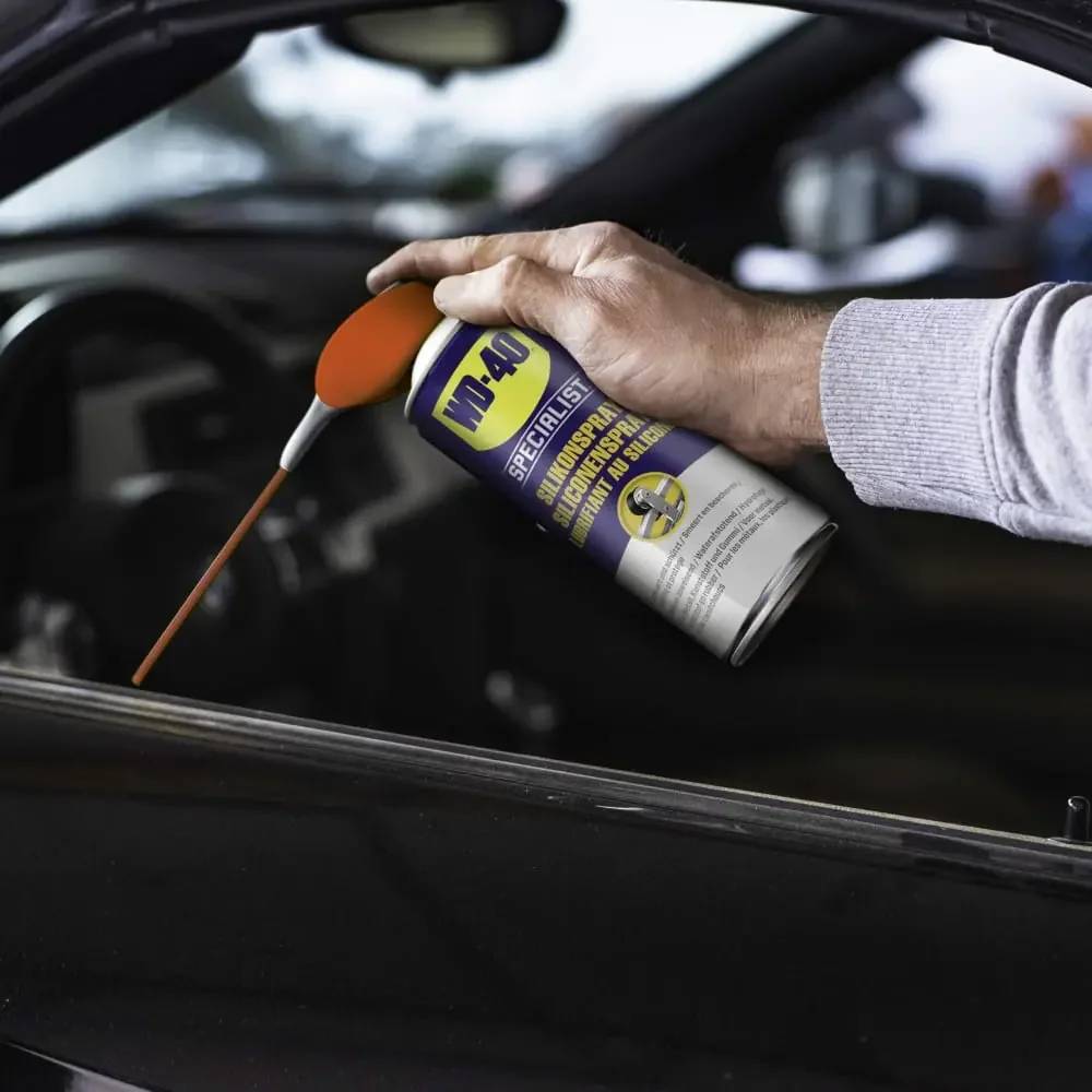 Mit der Hand Schmiermittel WD-40 auf eine Autofensterschiene im Inneren eines Fahrzeugs sprühen.