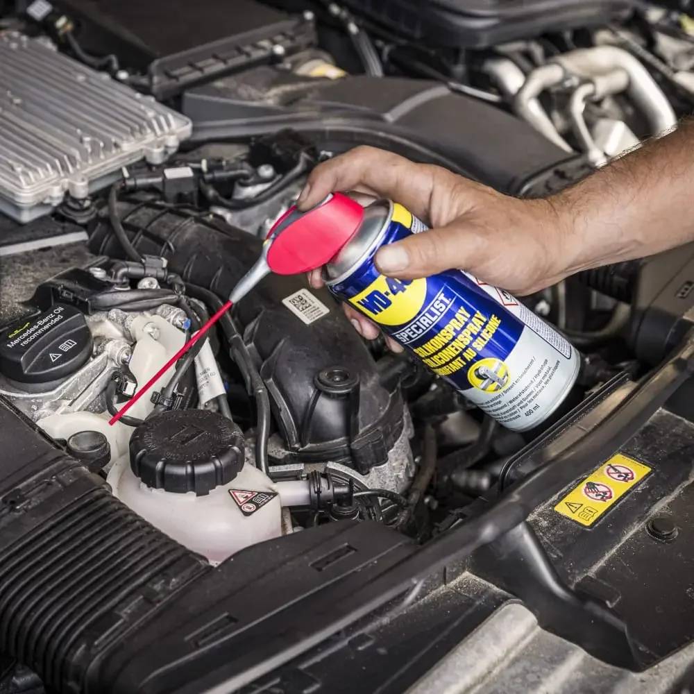 Mit einem roten Strohhalm-Applikator Schmiermittel per Hand in einen Automotorraum sprühen.