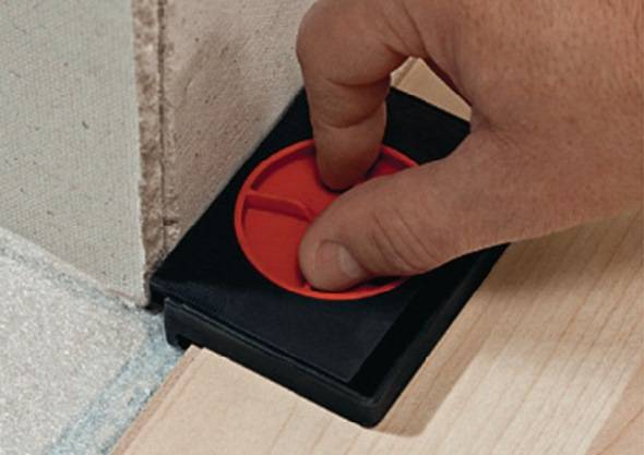 Eine Hand verwendet eine rote kreisförmige Wasserwaage auf einer schwarzen Basis an einer Wand und justiert die Bodenhöhe für präzise Installationsarbeiten.