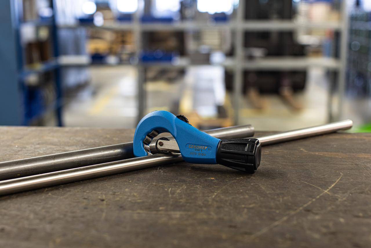 Ein blauer Rohrabschneider ist auf einem Arbeitstisch in einer Werkstatt an einem Metallrohr eingespannt. Regale und Werkzeuge sind im Hintergrund verschwommen.