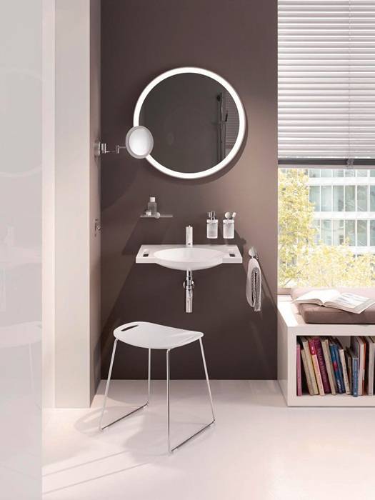 Modernes Badezimmer mit rundem Spiegel, wandmontiertem Waschbecken, Regalen mit Toilettenartikeln, einem kleinen Hocker und einem Fenster mit teilweise geöffneten Jalousien.