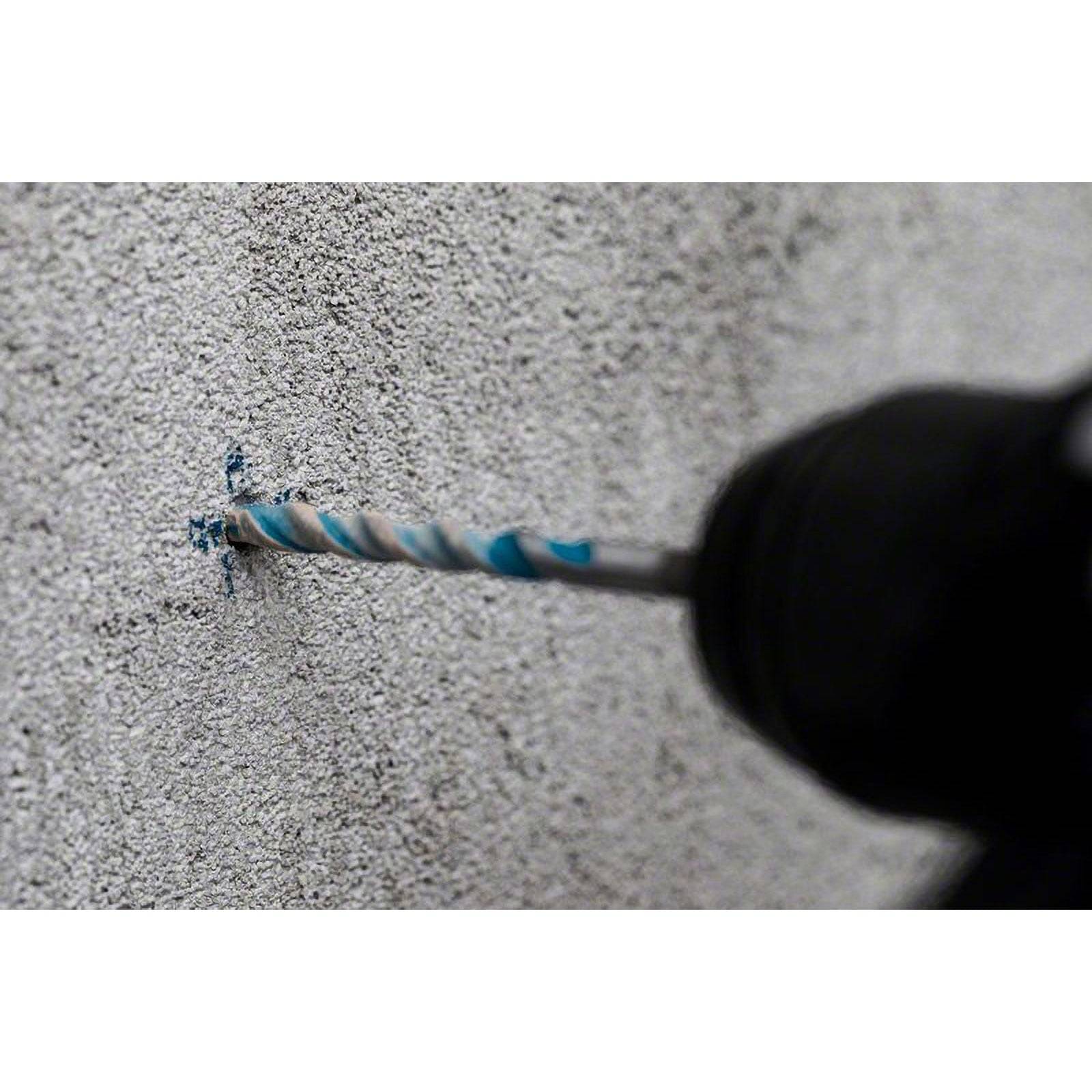Ein Bohrer mit einem blau-weiß gefärbten Bohraufsatz bohrt von der rechten Seite in eine raue Betonwand und veranschaulicht dabei eine Heimwerker- oder Bauaufgabe.