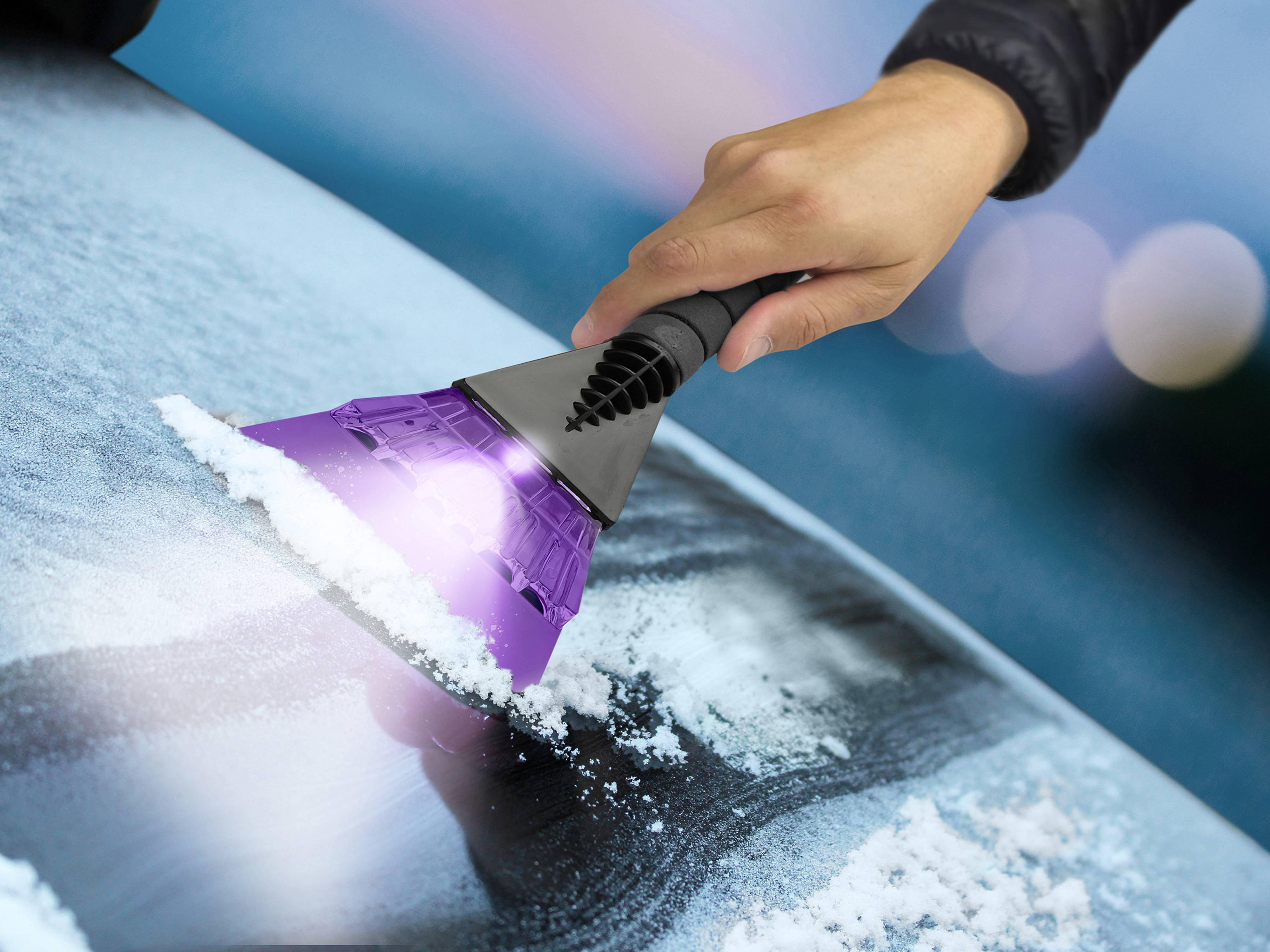 Eine Hand benutzt einen lila Eiskratzer, um Reif von einer Autoscheibe zu entfernen und zeigt damit die Wirksamkeit des Werkzeugs unter Winterbedingungen.