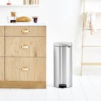Moderne Küche mit einem Edelstahl-Trittmülleimer neben einem Unterschrank aus hellem Holz auf weißem Boden.