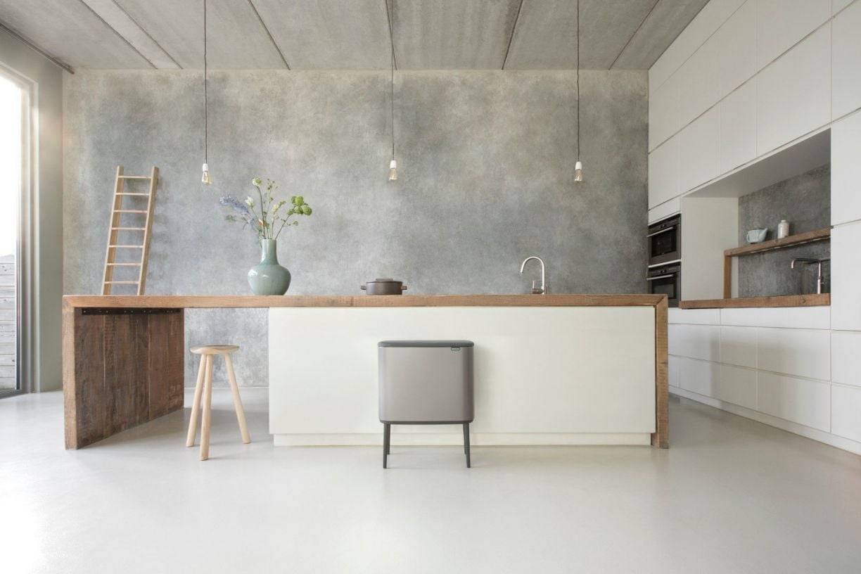 Moderne minimalistische Küche mit einer großen Insel, Barhocker, Pendelleuchten, Leiter und einer Blumenvase vor einer Betonwand.