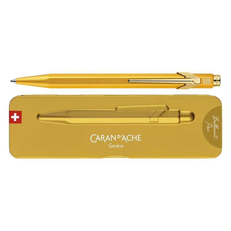 Ein goldfarbener Kugelschreiber mit elegantem Design, der über einer passenden goldenen Blechdose mit der Markenaufschrift 'CARAN d'ACHE Genève' mit Schweizer Flagge platziert ist.