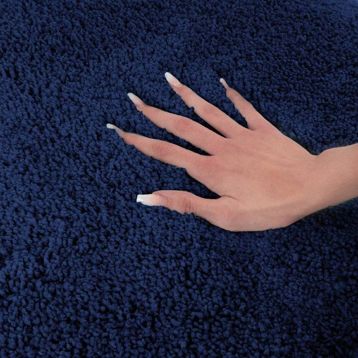 Eine Hand mit weißen Nägeln ruht auf einem strukturierten, dunkelblau gefärbten Teppich und zeigt dessen weiche und üppige Oberfläche.