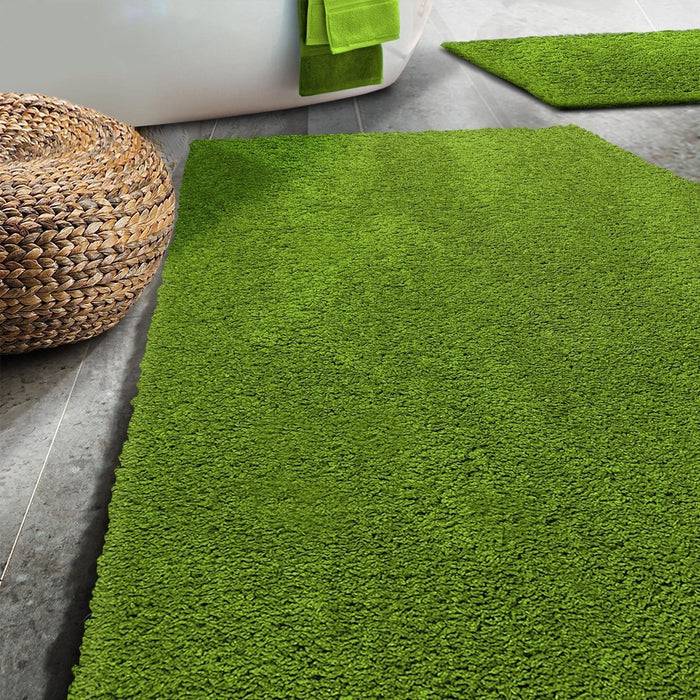 Ein Badezimmer mit grünen Teppichen auf einem grauen Fliesenboden, einem geflochtenen Korb und einem Handtuch, das am Rand einer weißen Badewanne hängt.