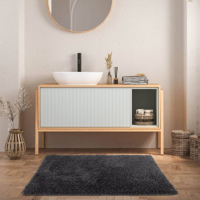 Eine moderne Waschtischanlage mit einem runden Spiegel über einem weißen Waschbecken auf einem hellholzfarbenen Schrank. Dekorative Gegenstände und Aufbewahrungskörbe sind sichtbar.