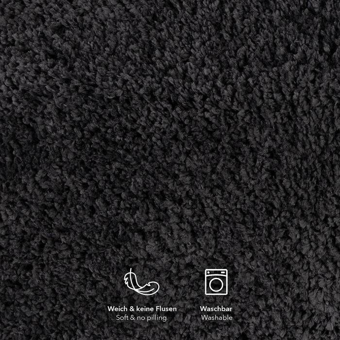 Nahaufnahme eines dunklen, strukturierten Stoffes mit Symbolen darunter. Symbole zeigen ‚weich, keine Fussel' und ‚waschbar' auf Deutsch.