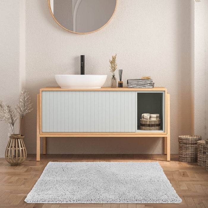 Ein modernes Badezimmer mit einem Waschtisch aus Holz, einem runden Spiegel, einem weißen Aufsatzbecken und dekorativen Vasen auf einem Parkettboden.