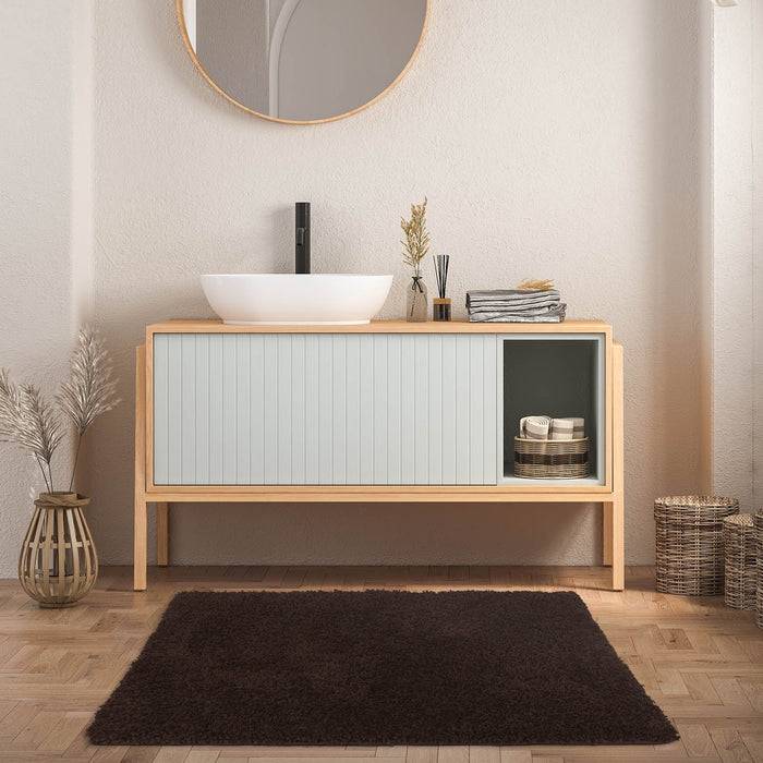 Ein modernes Badezimmer mit einem hellen Holzwaschbeckenunterschrank, weißem Aufsatzbecken, rundem Spiegel und minimalistischer Dekoration auf einem Holzfußboden.