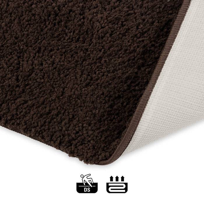 Eine Nahaufnahme eines weichen braunen Teppichs mit rutschfester Rückseite, auf der Symbole für Rutschfestigkeit und Eignung für Fußbodenheizung zu sehen sind.