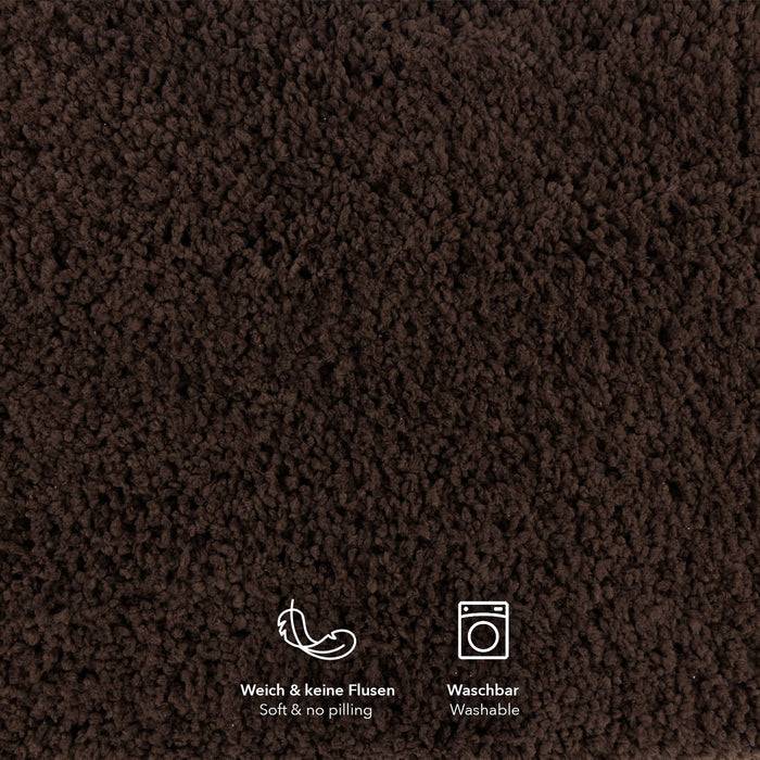 Eine Nahaufnahme eines dunkelbraunen strukturierten Gewebes mit weicher Erscheinung, mit Symbolen, die auf Deutsch und Englisch ‚Weich & keine Flusen' und ‚Waschbar' anzeigen.