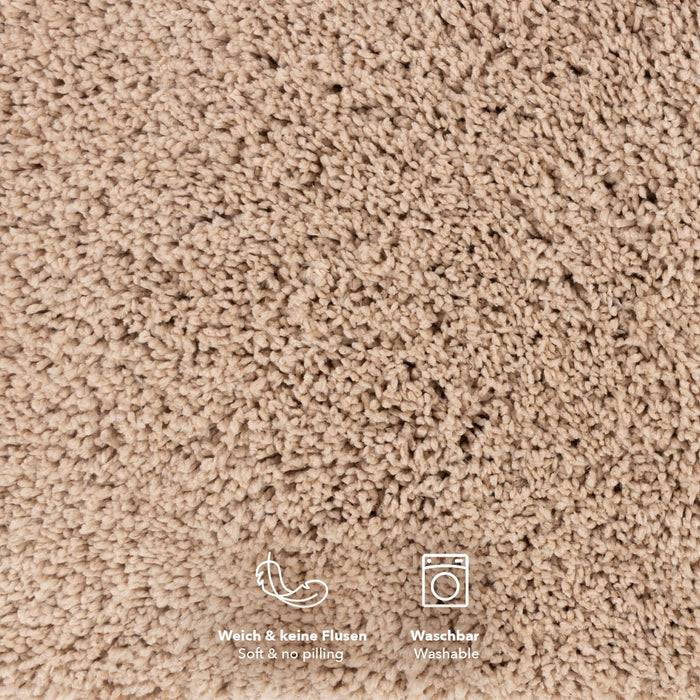 Beige strukturierte Teppichoberfläche mit zwei kleinen Symbolen am unteren Rand, die 