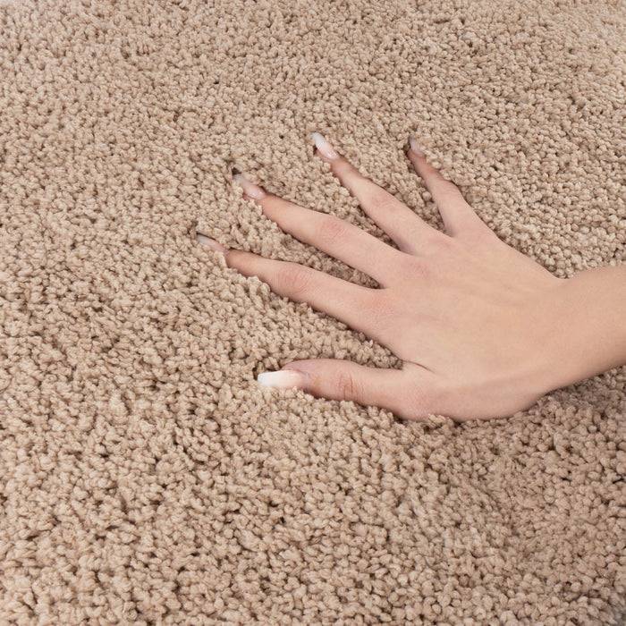 Eine Hand mit langen Nägeln wird auf einen beigen Teppich gelegt, wodurch die Textur und Weichheit der Teppichfasern zur Geltung kommt.