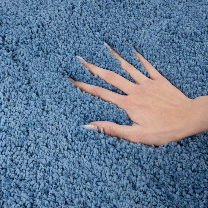 Eine Hand berührt einen weichen blauen Teppich, die Finger leicht gespreizt, wobei die Textur und Weichheit des Materials hervorgehoben werden.