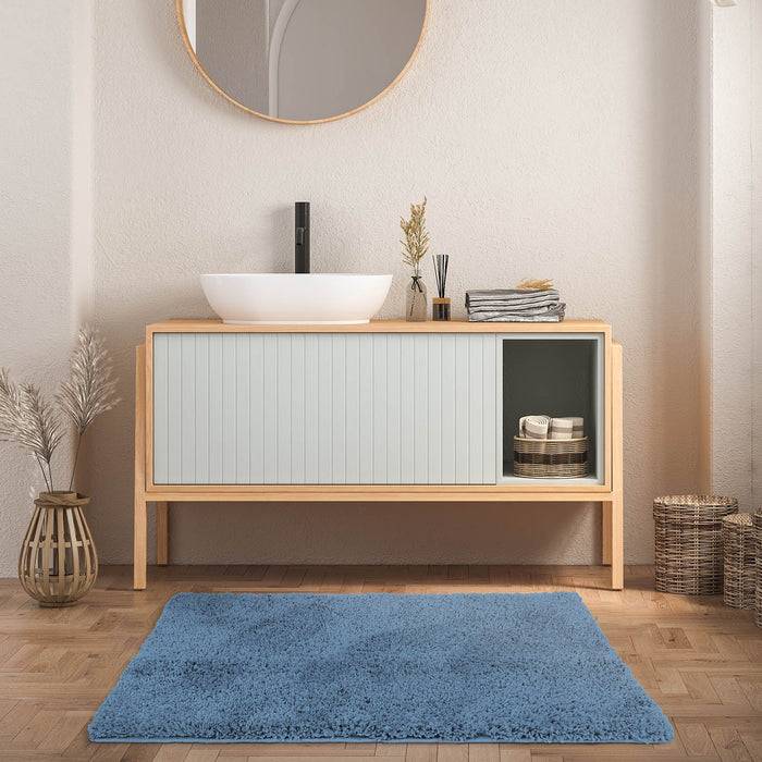 Ein modernes Badezimmer mit einem weißen Waschbecken auf einem hellen Holzwaschtisch, einem runden Spiegel darüber, getrockneten Pflanzen in Vasen und einem blauen Teppich auf dem Boden.