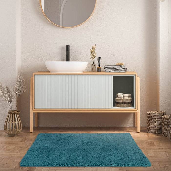 Eine moderne Badezimmereinrichtung mit einem Holzwaschtisch, weißem Waschbecken und schwarzer Armatur unter einem runden Spiegel. Die Dekoration umfasst Körbe und einen blauen Teppich.