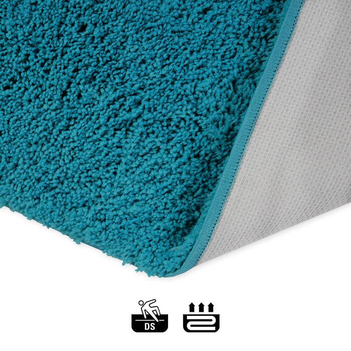 Ein petrolblauer Teppich mit strukturierter Florhöhe wird gezeigt, mit Pflegesymbolen darunter, die andeuten, dass er für Böden und beheizte Oberflächen geeignet ist.