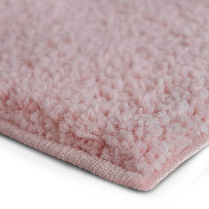 Nahaufnahme einer weichen, flauschigen Ecke eines rosa Teppichs, die dessen üppige Textur und Randdetails zeigt.