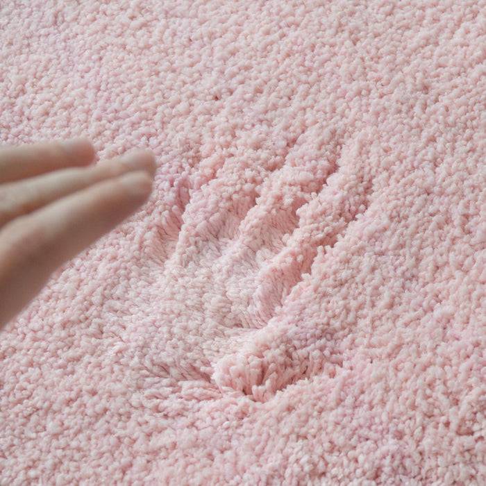 Eine Hand berührt die Oberfläche eines weichen, flauschigen rosa Teppichs und hinterlässt eine Vertiefung im Material.