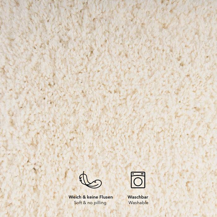 Eine Nahaufnahme eines weichen, cremefarbenen Textils mit flauschiger Textur. Symbole darunter zeigen ‚Weich & keine Fussel' und ‚Waschbar'.