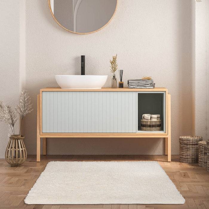 Badezimmerwaschtisch mit rundem Spiegel, Aufsatzbecken und Wasserhahn. Helle Holzakzente, dekorative Vasen, Korb und ein kleiner weißer Teppich.