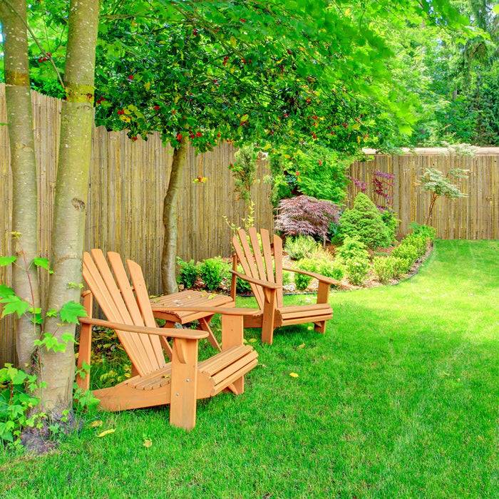 Zwei hölzerne Stühle und ein kleiner Tisch stehen in einem üppig grünen Garten, umgeben von lebendigen Pflanzen und einem Holzzaun.