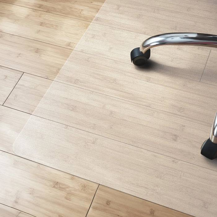 Eine durchsichtige Bodenschutzmatte auf einem hellholzfarbenen Boden mit einem sichtbaren Teil des Rädchens eines Bürostuhls.