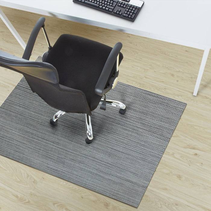 Bürostuhl auf einer grauen Matte, von oben betrachtet neben einem Schreibtisch mit einer Tastatur, auf einem Holzboden.