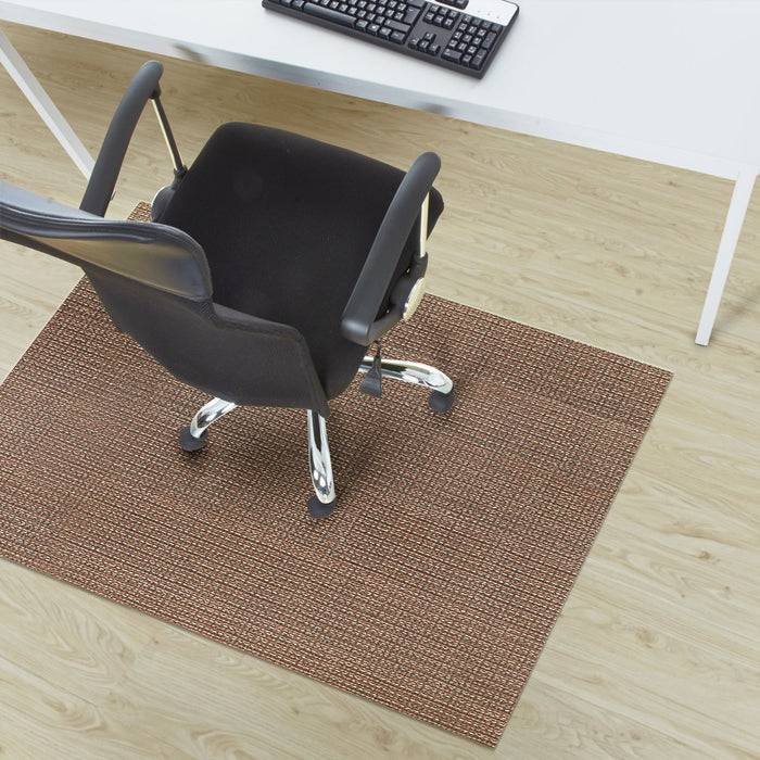 Bürostuhl auf einer braunen Matte neben einem weißen Schreibtisch mit einer Tastatur. Der Stuhl ist vom Schreibtisch abgewandt und auf einem Holzboden positioniert.