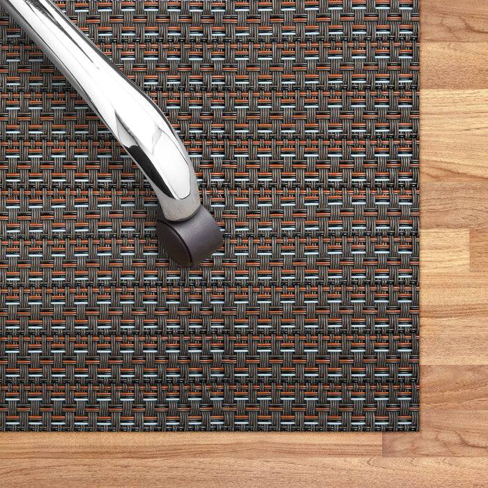 Ein Bürostuhl auf einer strukturierten Matte mit einem gewebten Muster auf einem Holzboden, wobei das Design der Matte und der Schutzzweck des Bodens hervorgehoben werden.