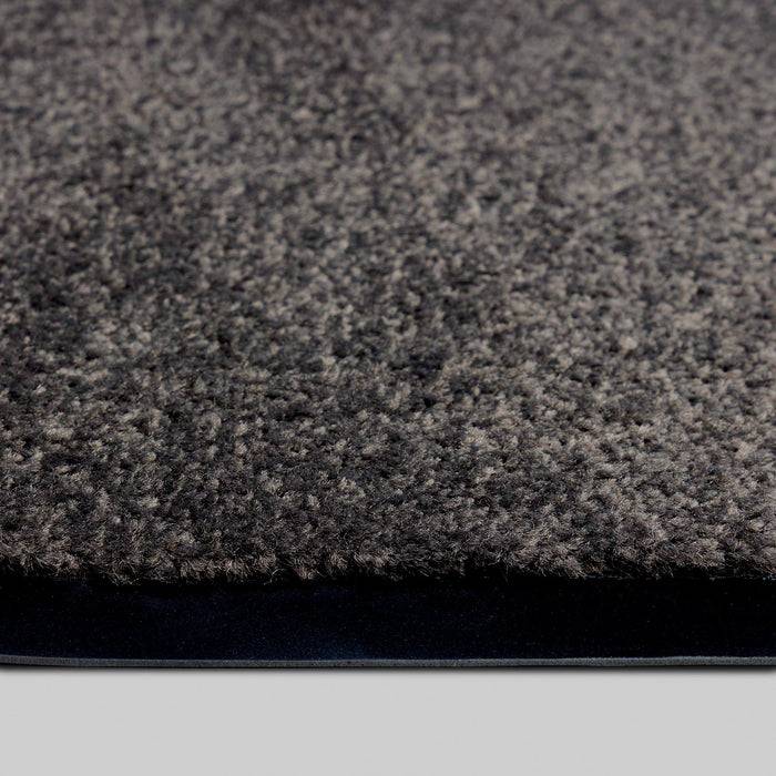 Ein Nahaufnahmebild eines strukturierten grauen Teppichs, das die detaillierten Fasern und eine leichte Erhebung über einem glatten schwarzen Untergrund zeigt.