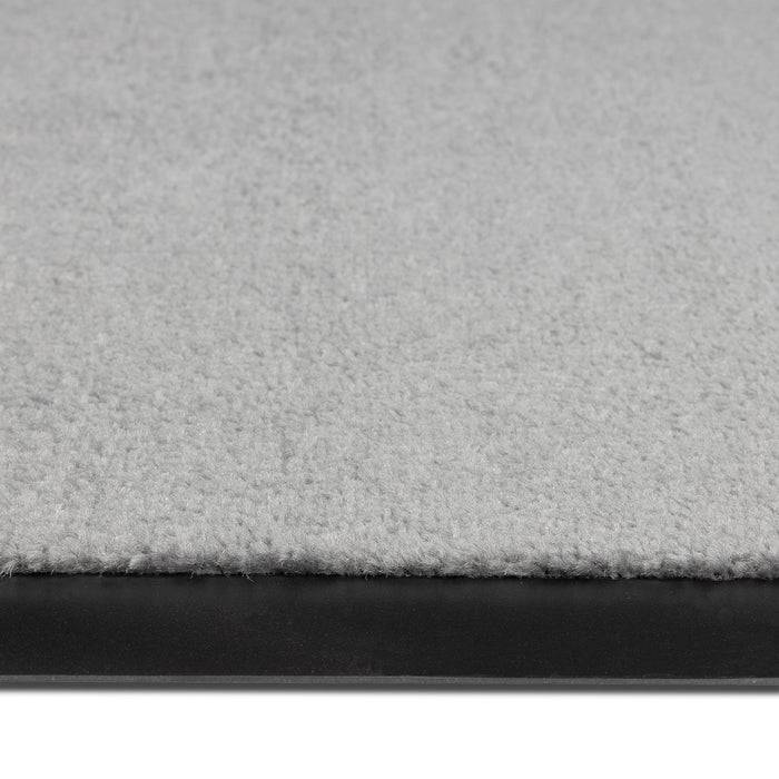 Eine Nahaufnahme eines hellgrauen Teppichs mit schwarzer Gummikante, die strukturierte Fasern und Polsterung zeigt.