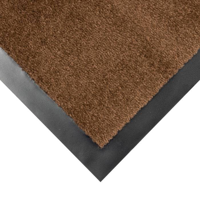 Eine Ecke einer braunen, strukturierten Bodenmatte mit schwarzem Gummirand, die auf einer ebenen Fläche liegt.