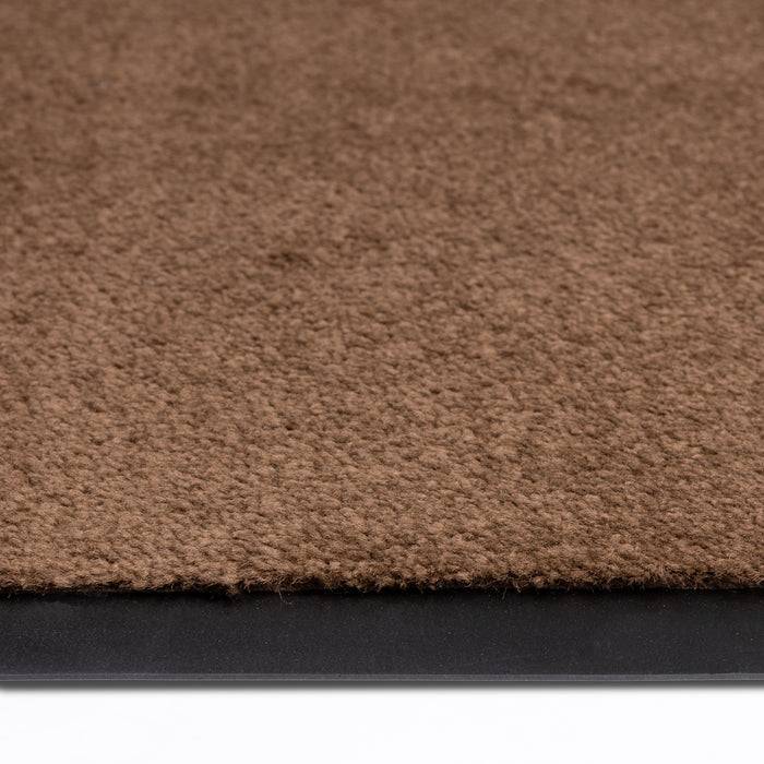 Eine braune Bodenmatte mit schwarzem Gummirand liegt auf einer weißen Oberfläche und zeigt Textur- und Materialkontrast.